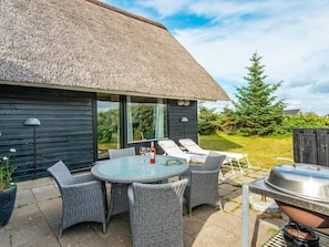 A thatched-roof outdoor dining area with wicker furniture and a grill.