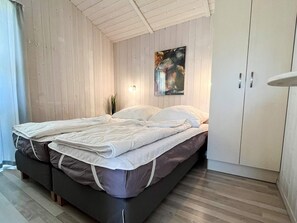 A bedroom with a bed, wooden walls, a painting, and a wardrobe.