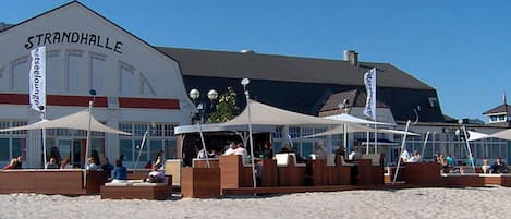 Un restaurante junto a la playa llamado Strandhalle, con mesas al aire libre y sombrillas.