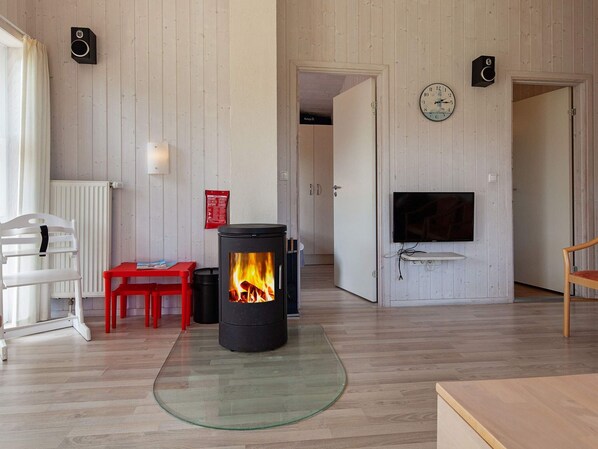 A room with a wood-burning stove, a television mounted on the wall, and a red chair.