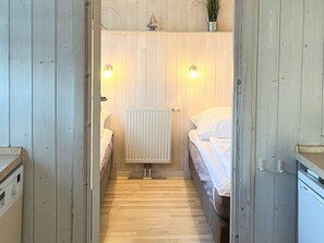Corredor estreito que dá para um quarto, com cama, radiador e duas luzes na parede.