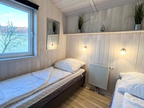 A small, single-bed room with wooden paneling, a window, and a radiator.