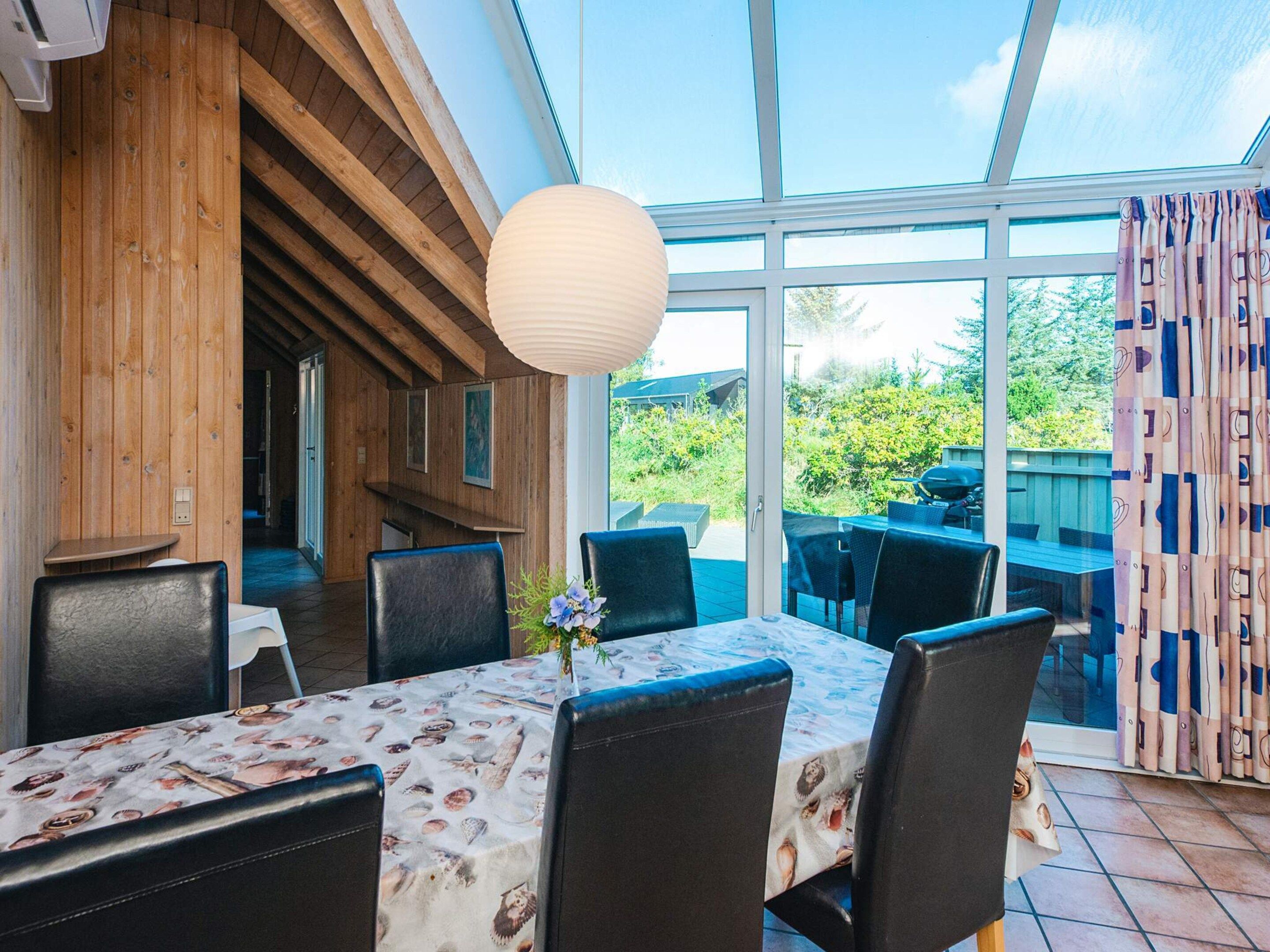 A dining area with a table covered in a patterned tablecloth, surrounded by chairs.