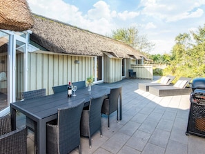 Un espacio de patio al aire libre con mesa y sillas, una parrilla y una estructura de techo de paja.