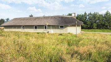 Un bâtiment d’un seul étage, doté d’un toit de chaume, entouré d’herbes hautes et d’arbres.