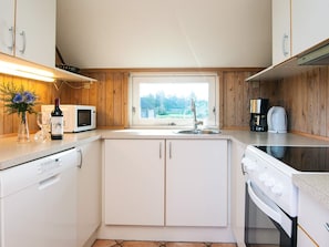 Cocina compacta con gabinetes blancos, microondas, fregadero, estufa y cafetera.