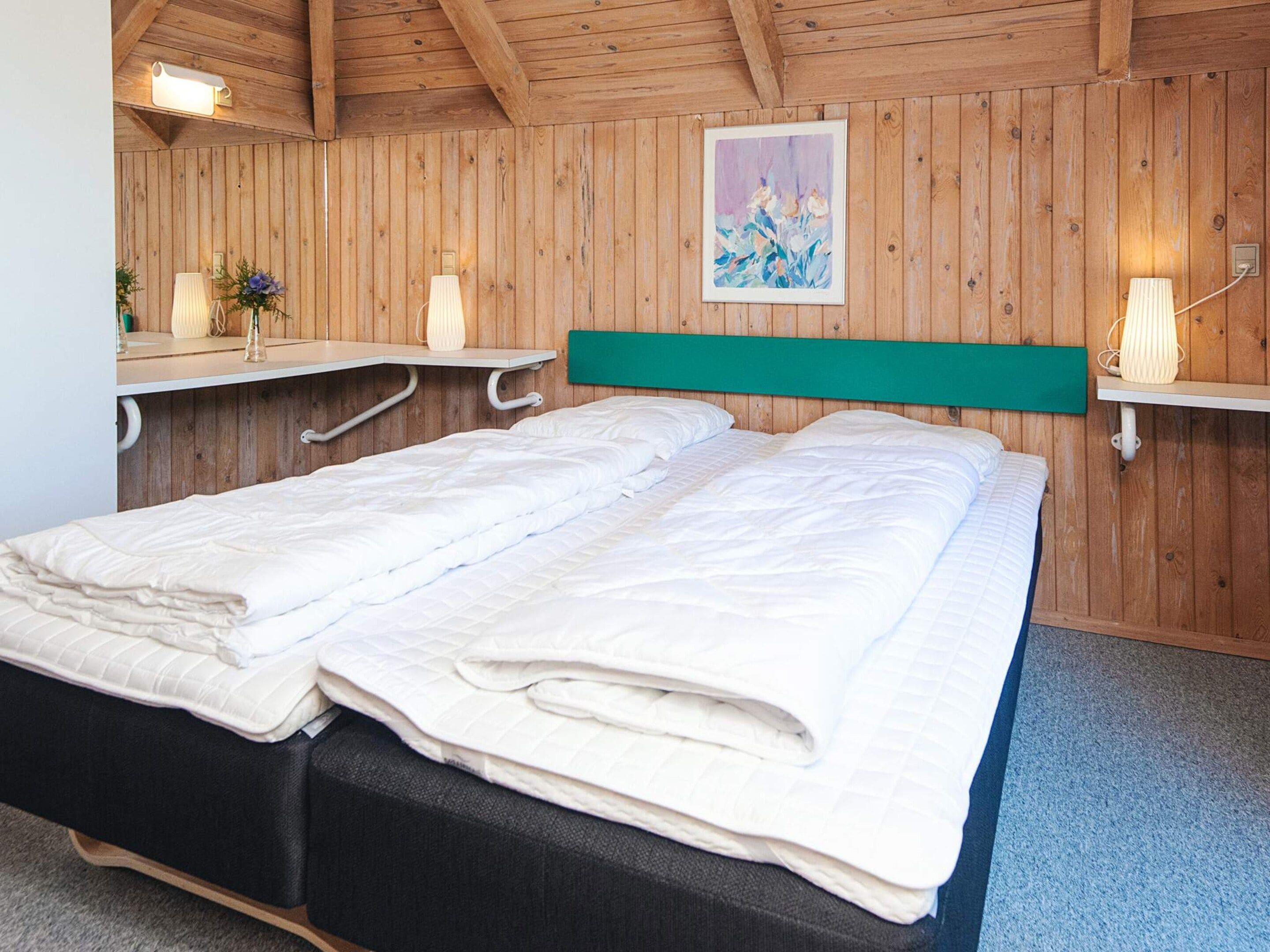 A double bed with a green headboard in a wooden room with a sloped ceiling.