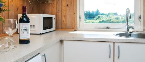 A kitchen with a microwave, wine bottle, and wine glass on the counter, a window with a view of greenery, and a dishwasher.