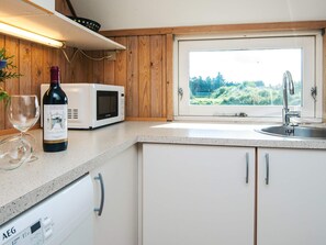 A kitchen with a microwave, wine bottle, and wine glass on the counter, a window with a view of greenery, and a dishwasher. - 4 Star Holiday Home in Vejers Strand (Vejers Strand)