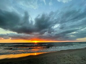 Una playa con olas, un atardecer y un cielo nublado.