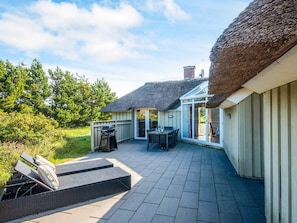 A patio area with a thatched roof, a dining table, and outdoor seating. - 4 Star Holiday Home in Vejers Strand (Vejers Strand)