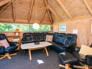 Ein gemütliches Zimmer mit Holzbalkendecke, einem schwarzen Ledersofa, einem Holztisch und einem Bücherregal mit Büchern.