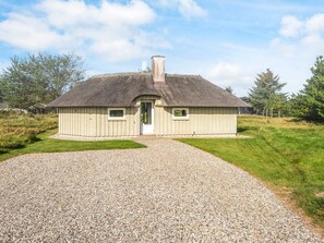A single-story building with a thatched roof, a gravel driveway, and a small front porch. - 4 Star Holiday Home in Vejers Strand (Vejers Strand)