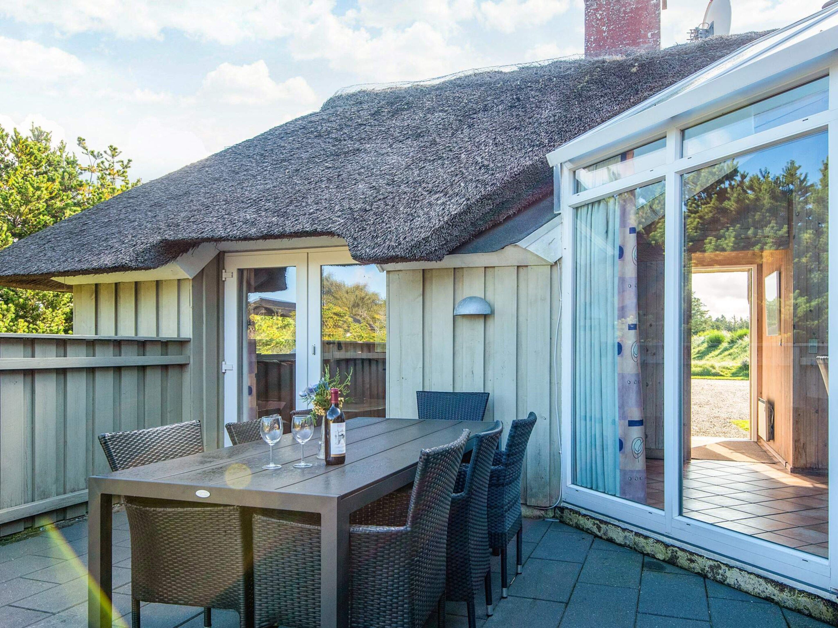 A patio with a table and chairs, a thatched roof, and a sliding glass door leading to a garden.