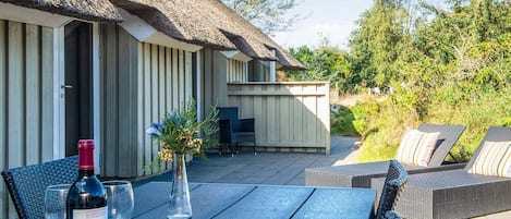 A patio area with a table set for dining, outdoor seating, and a thatched-roof structure.
