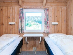 A wooden cabin room with two beds, a window with curtains, and a small table. - 4 Star Holiday Home in Vejers Strand (Vejers Strand)