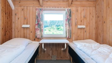 A room with two beds, a window with curtains, and a small table.