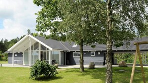 Ein modernes Haus mit überdachter Terrasse, großem Rasen und Schaukeln.