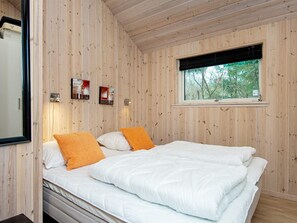 A bedroom with a wooden paneled wall, a bed with white bedding and orange pillows, a window with a view of trees, and two wall-mounted light fixtures. - Luxury Spa Retreat in Nature - By Traum Ferienwohnungen (Silkeborg)