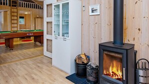Ein Holzinnenraum mit Pooltisch, einer Schranke mit Glastüren, Kamin und einer Leiter zu einer erhöhten Ebene.