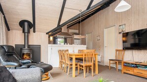 Un salon chaleureux avec une cheminée, un canapé, un coin repas avec des chaises en bois et un téléviseur.