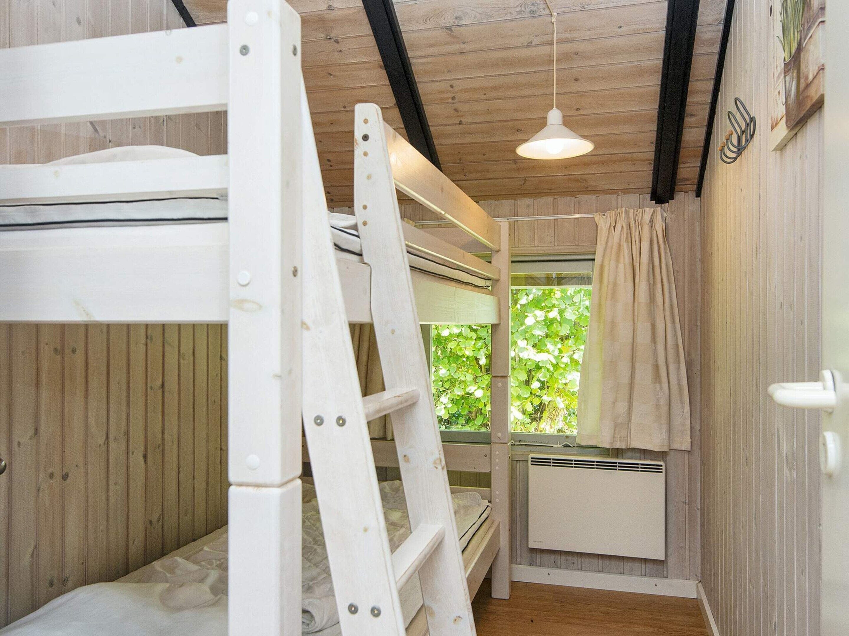 A bunk bed room with a ladder, a window with a curtain, and a radiator.