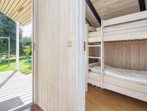 Quarto com beliches, teto e paredes de madeira, porta que dá para o exterior e área de jardim visível.