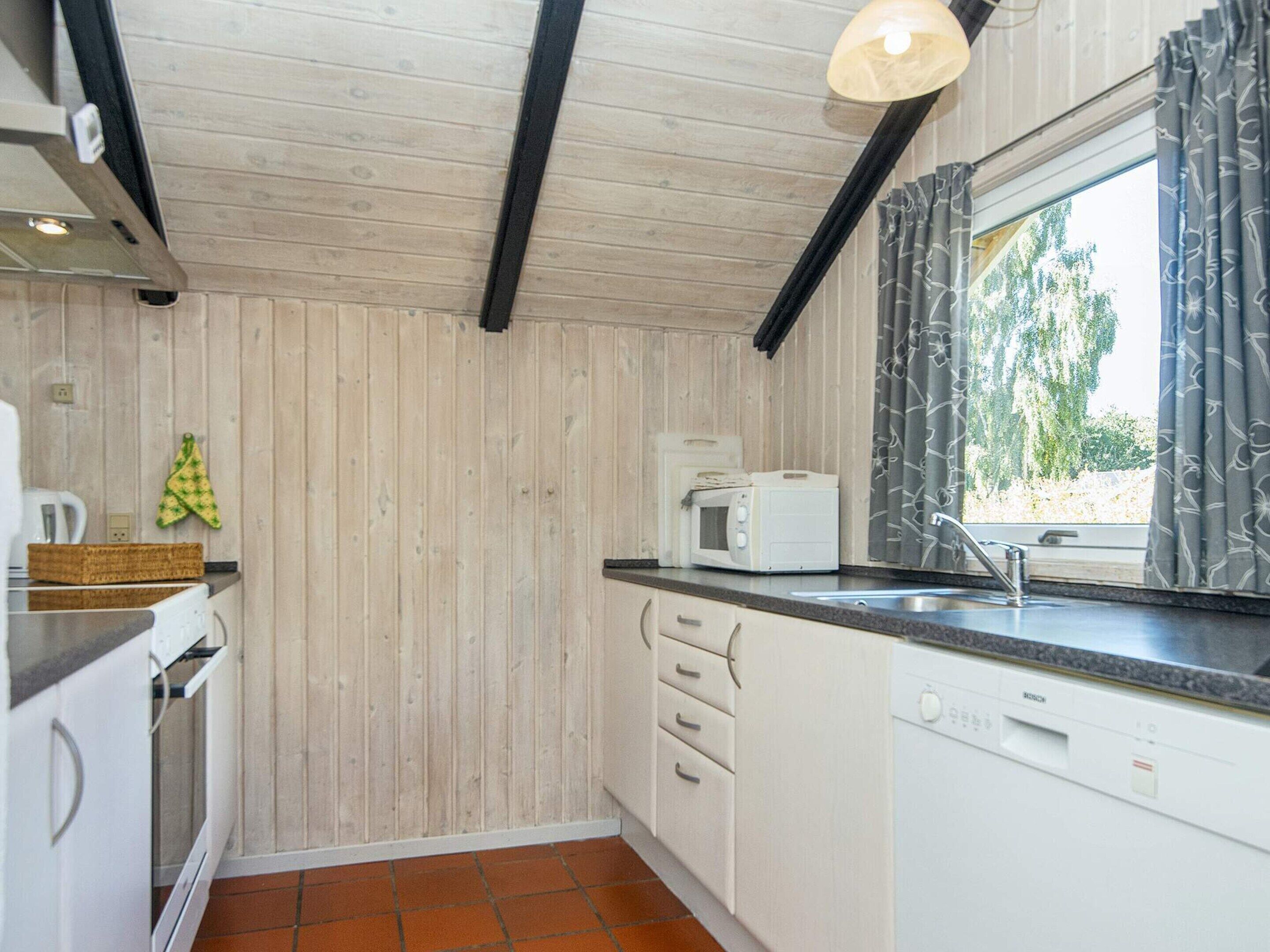 Een kleine keuken met houten wanden, een magnetron, een gootsteen en een raam met gordijnen.