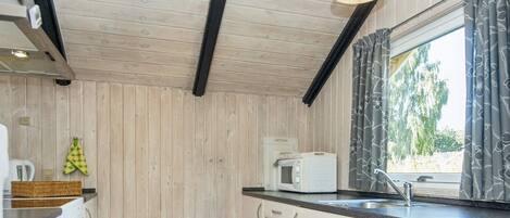 A compact kitchen with wooden walls, a microwave, a sink, and a window with curtains.