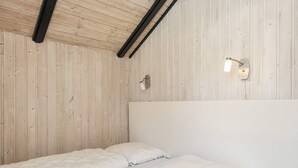 Un lit simple avec un matelas et des oreillers blancs, dans une pièce aux murs lambrés et au plafond en pente.