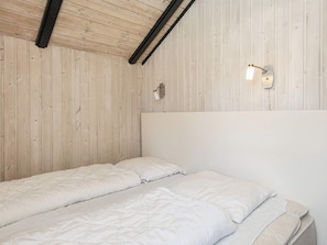 Una cama individual con colchón y almohadas en una habitación con paneles de madera y techo inclinado.