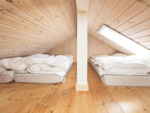 Um quarto de sótão pequeno, com painéis de madeira, duas camas e um claraboia.