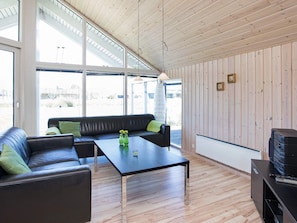 A modern interior with a black leather sofa, a wooden coffee table, and a large window providing a view of the outdoors.