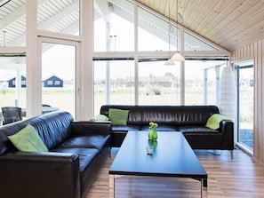 A spacious room with a large window, a black leather sofa, a wooden coffee table, and a hanging pendant light. - 5 Star Holiday Home in Idestrup (Idestrup)