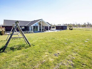 A residential property with a large open lawn, a wooden deck, and a house with a tiled roof. - 5 Star Holiday Home in Idestrup (Idestrup)