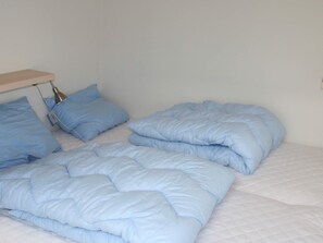 A bed with a blue quilt and pillows, a bedside table with a lamp, and a plain wall. - 6 Person Holiday Home in Gudhjem (Gudhjem)