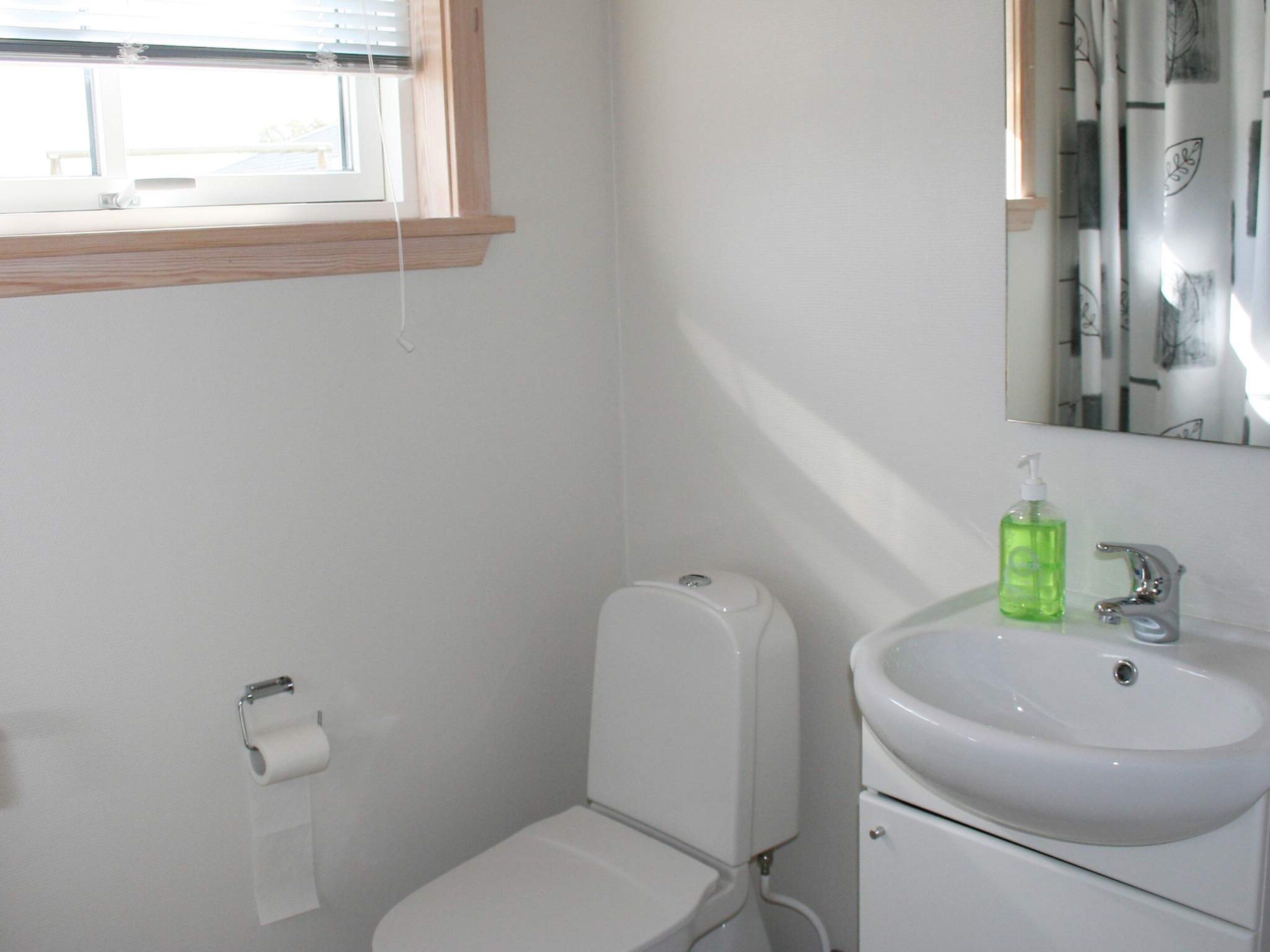 Ein Badezimmer mit Toilette, Waschbecken, Spiegel und einem Fenster mit Jalousien.