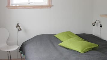 A room with a bed, a chair, a window, and a wall-mounted lamp.