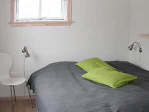 A room with a bed, a chair, a window, and a wall-mounted lamp. - 6 Person Holiday Home in Gudhjem (Gudhjem)