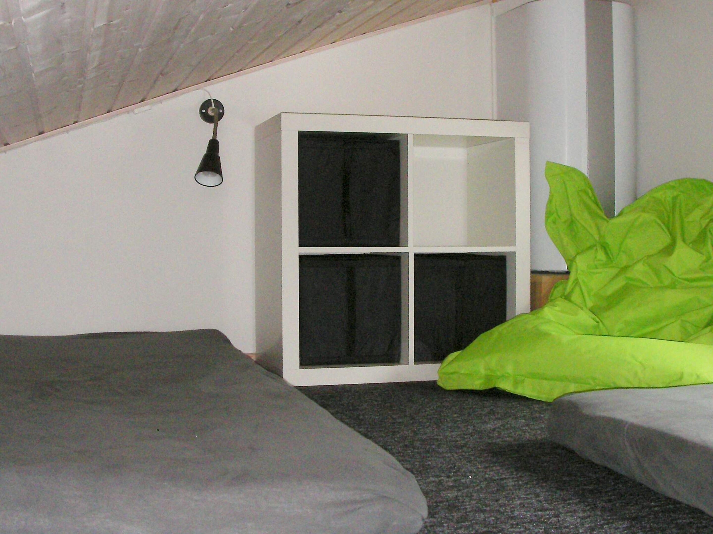 Una habitación pequeña, con poca luz, que tiene una cama individual, un armario blanco y una almohada verde.
