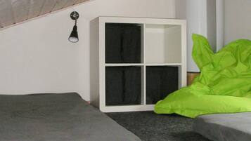 Una habitación pequeña, con poca luz, que tiene una cama individual, un armario blanco y una almohada verde.