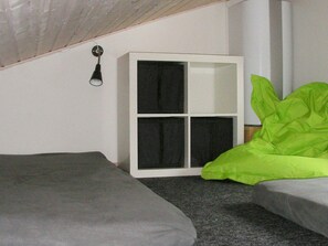 A small, dimly lit room with a single bed, a white cabinet, and a green pillow. - 6 Person Holiday Home in Gudhjem (Gudhjem)