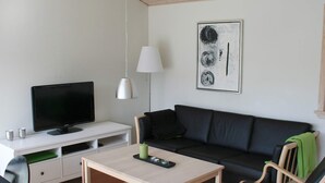 A modern living room with a flat-screen TV, a sofa, a coffee table, and a lamp. - 6 Person Holiday Home in Gudhjem (Gudhjem)