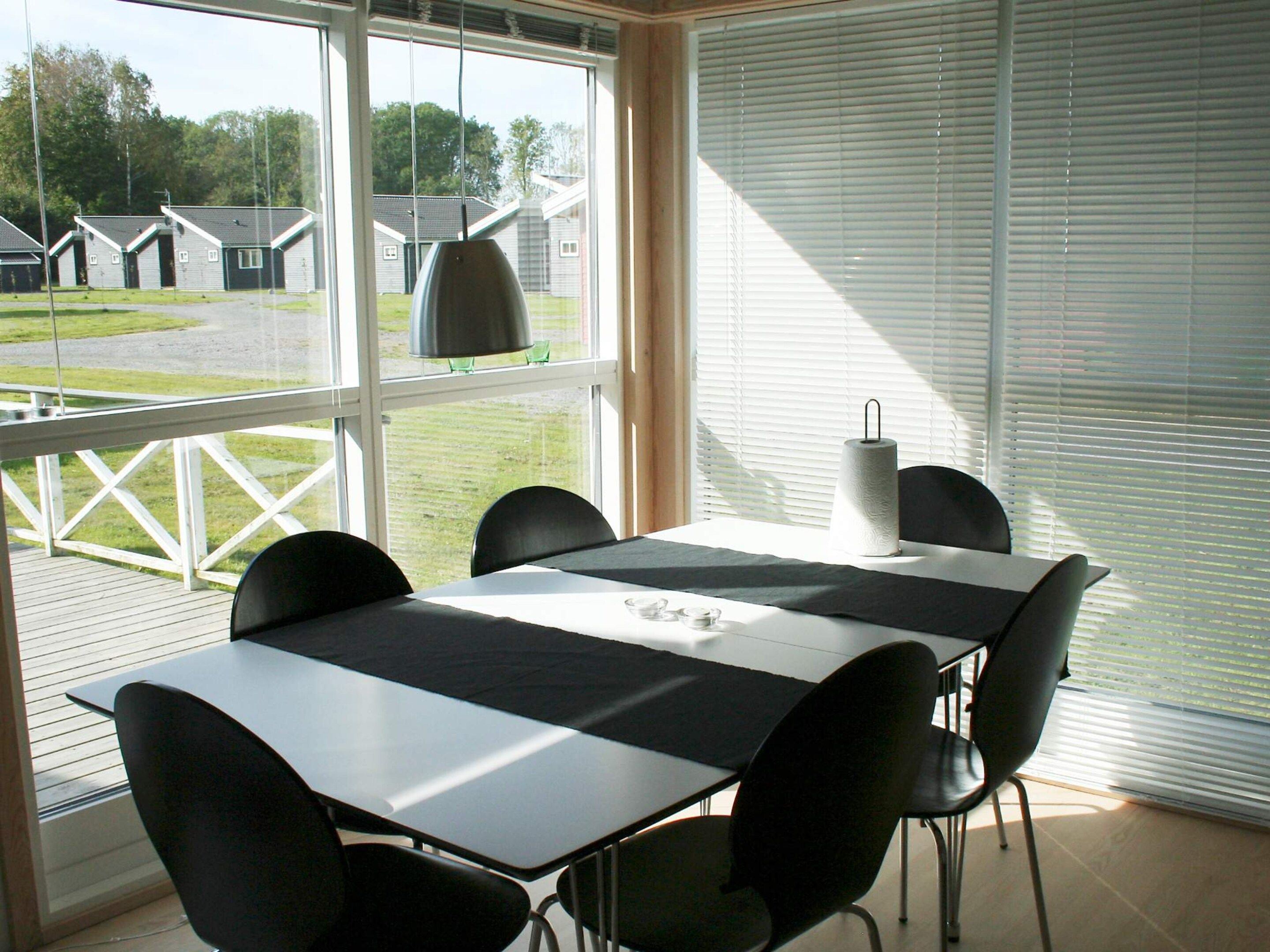 A room with a table and chairs, large windows, and a view of outdoor buildings.