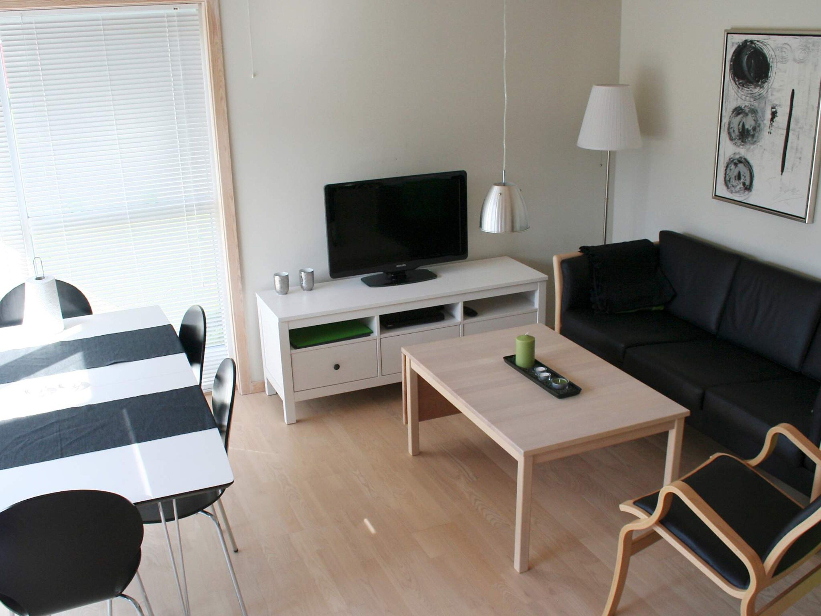 Een moderne woonkamer met een flatscreen televisie, een bank, een salontafel en een eethoek met een gestreepte tafel en stoelen.