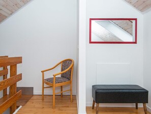 A room with a wooden bench, a chair with a patterned cushion, and a dark-colored bench against a white wall with a red-framed mirror. - 4 Person Holiday Home in Fano (Fano)