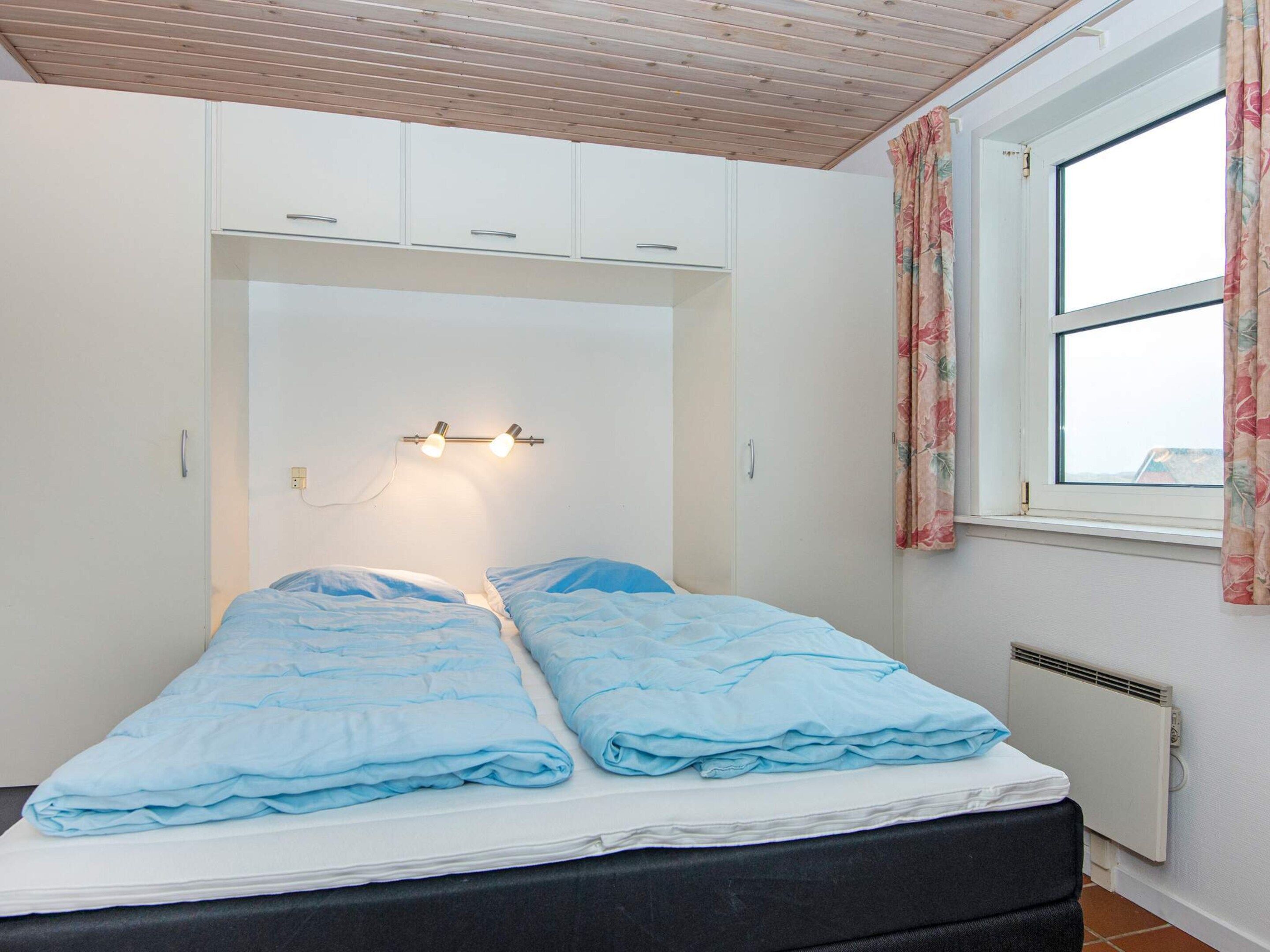 Een slaapkamer met een bed, een kledingkast, een raam met gordijnen en een wandlamp.