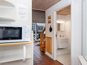 A modern kitchen with a built-in microwave, a wooden staircase, and a white bathroom with a mirror and sink. - 6 Person Holiday Home in Fano (Fano)