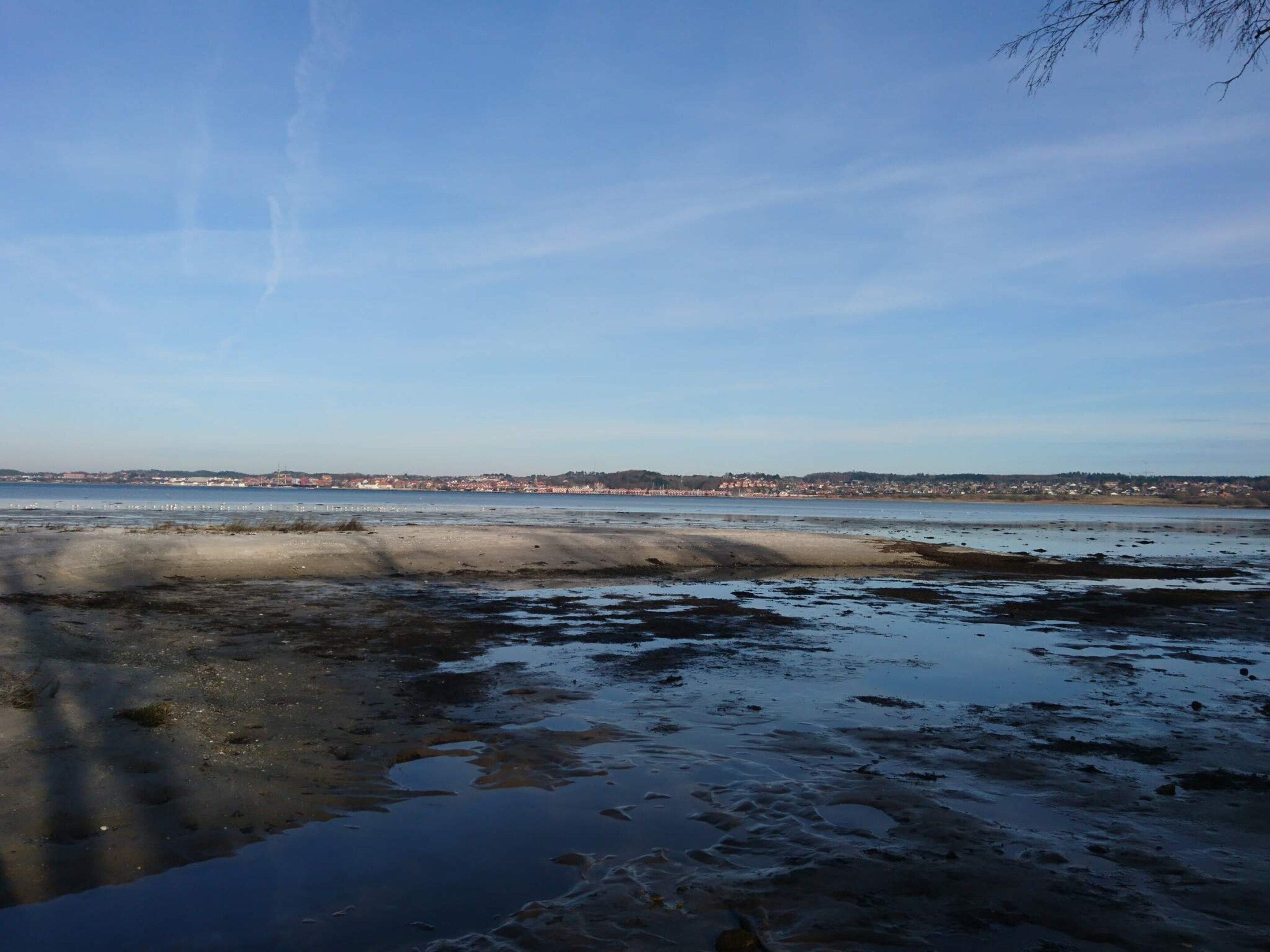 A coastal landscape with a sandy beach, calm water, and a distant town.