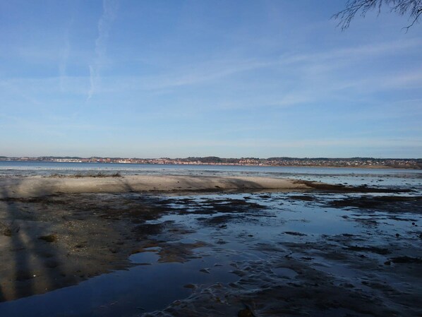 Un paysage côtier avec une plage de sable, une eau calme et une ville située au loin.